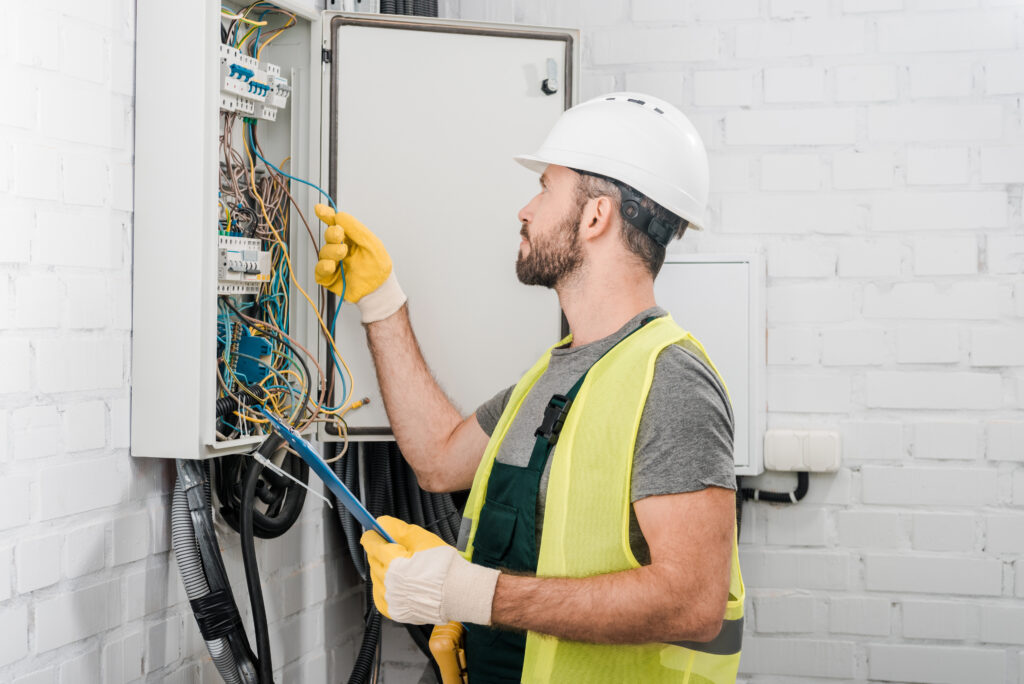 side view of electrician holding clipboard and checking wires in electrical box in corridor. Certified Electrical Inspections