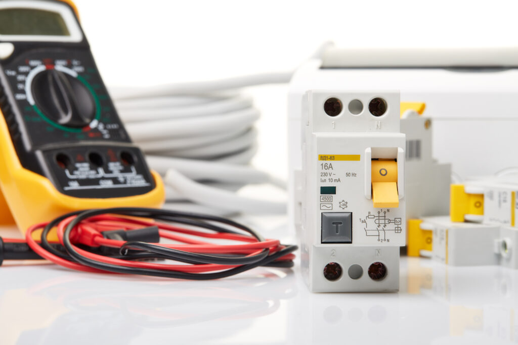 Automatic circuit breakers, distribution box, cables, and a digital tester on a white background, showcasing electrical equipment for Electrical Code Compliance, including accessories for electrical protection and control.